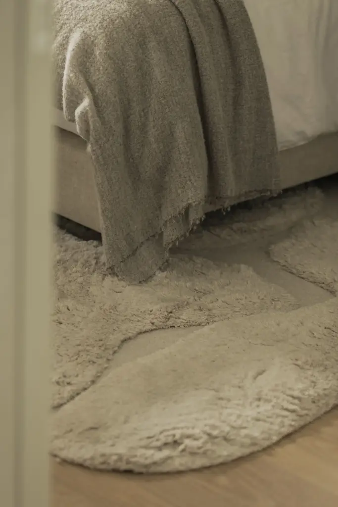 Detail van een linnen plaid en wollen tapijt in de slaapkamer, Compact appartement in Knokke, interieur Laura Calleeuw