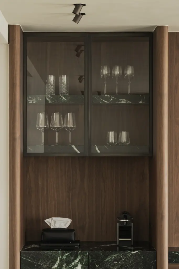 Vitrinekast met glazen deuren, walnoot en wijnglazen naast marmer, Compact appartement in Knokke, interieur Laura Calleeuw