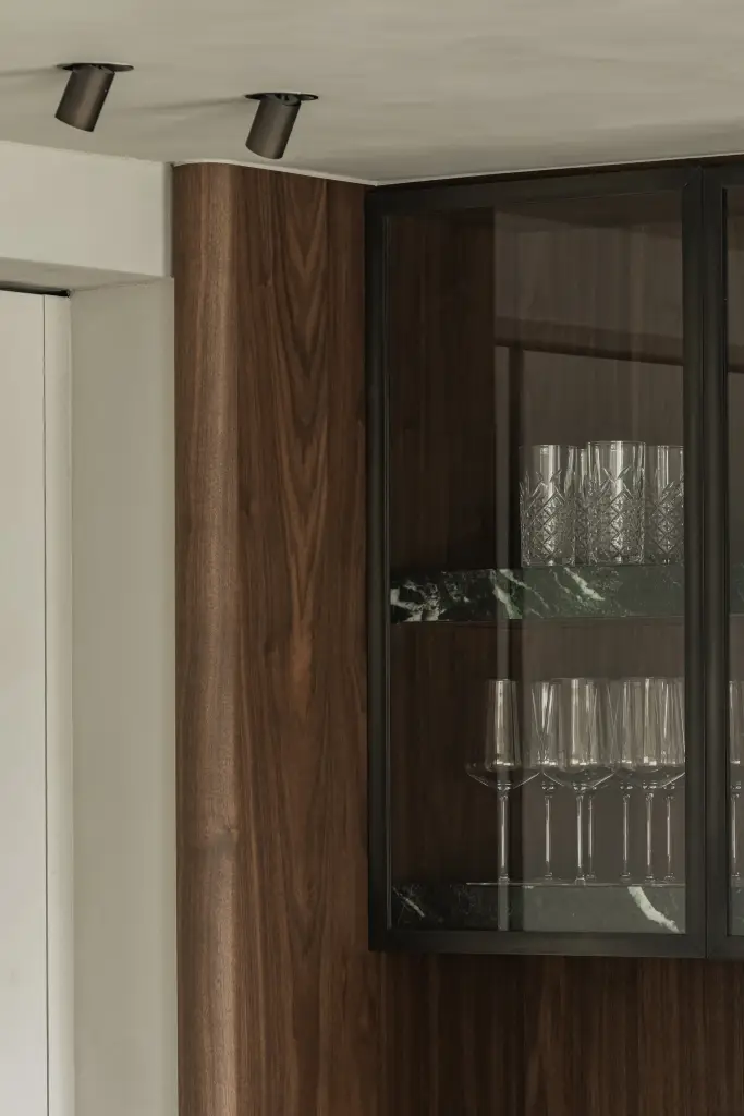 Vitrinekast met glazen deuren, walnoot en wijnglazen naast marmer, Compact appartement in Knokke, interieur Laura Calleeuw