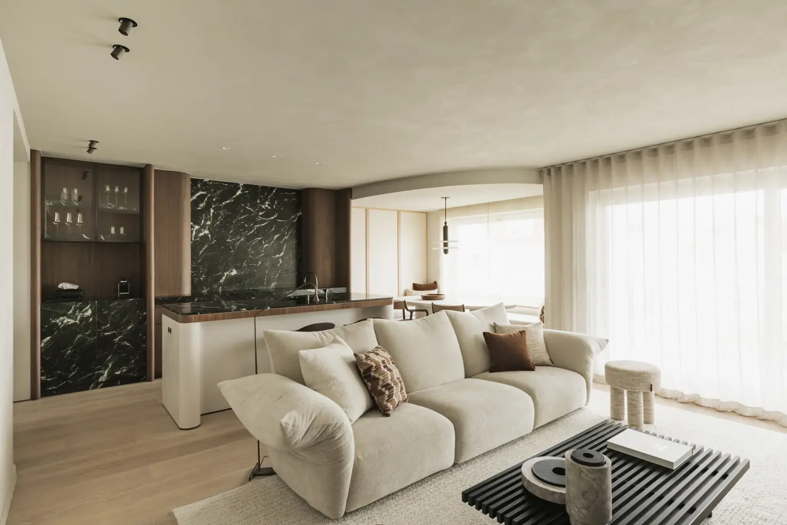 Open leefruimte met zithoek, groen marmeren keuken en dubbel gordijn, Compact appartement in Knokke, interieur Laura Calleeuw