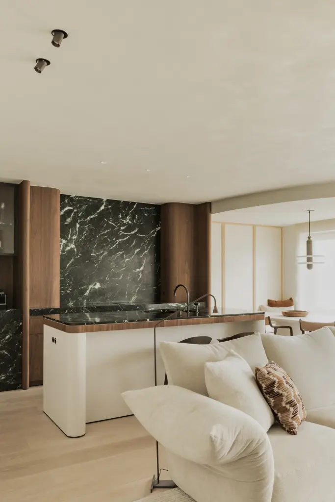 Open leefruimte met zithoek, groen marmeren keuken en dubbel gordijn, Compact appartement in Knokke, interieur Laura Calleeuw