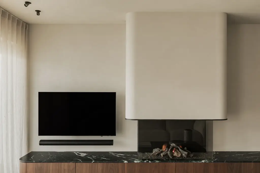 Woonkamer met televisie boven een open haard met marmeren blad en walnoten onderkast, Compact appartement in Knokke, interieur Laura Calleeuw