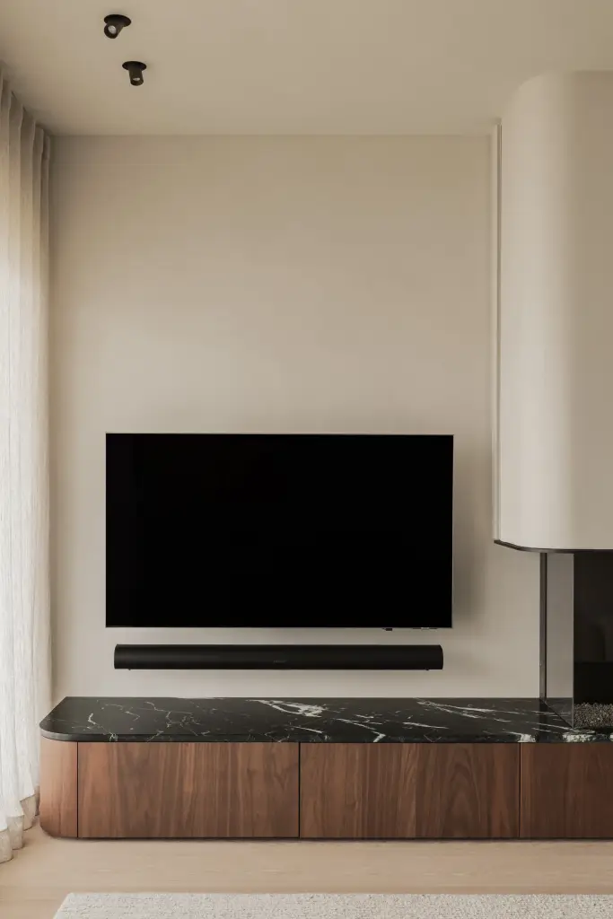 Woonkamer met televisie boven een open haard met marmeren blad en walnoten onderkast, Compact appartement in Knokke, interieur Laura Calleeuw