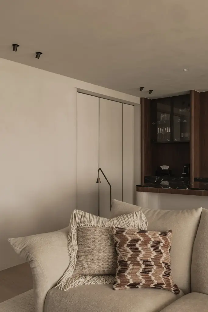 Zetel met sierkussens en staande leeslamp naast een kast met glazen deuren, Compact appartement in Knokke, interieur Laura Calleeuw