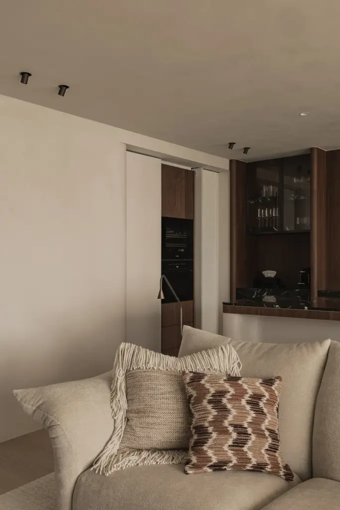 Zetel met sierkussens en staande leeslamp naast een kast met glazen deuren, Compact appartement in Knokke, interieur Laura Calleeuw