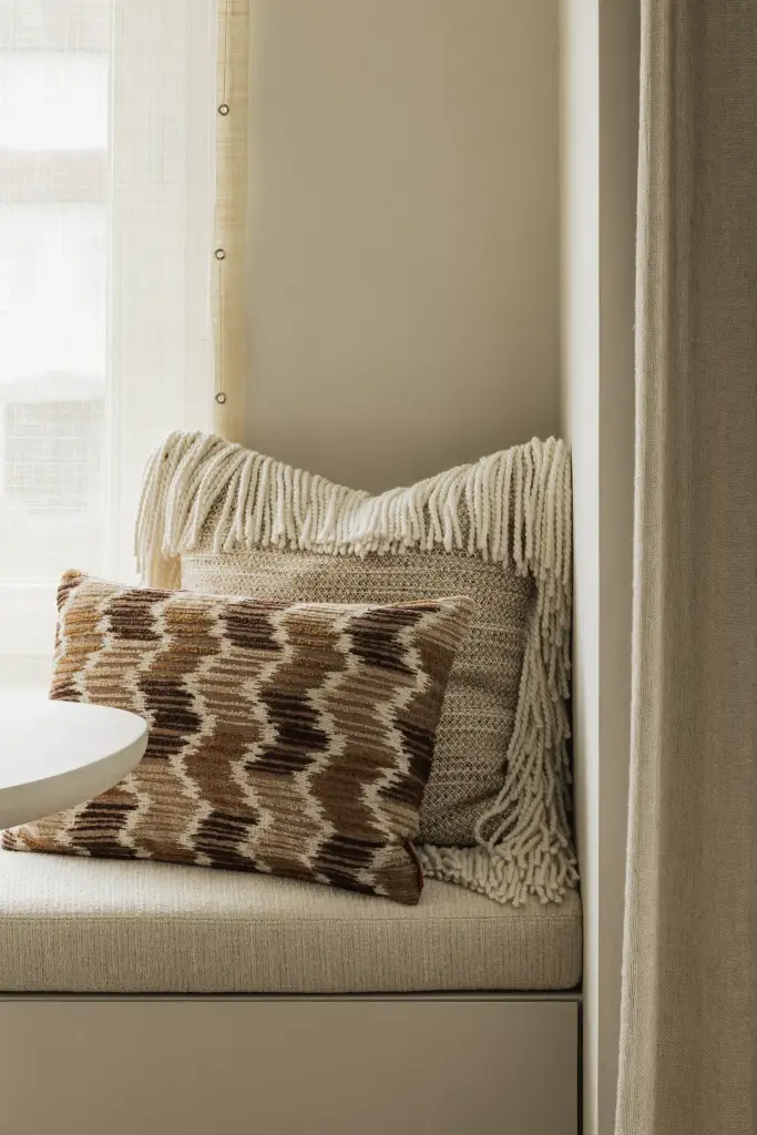 Zitbank met gebreide sierkussens met franjes, Compact appartement in Knokke, interieur Laura Calleeuw