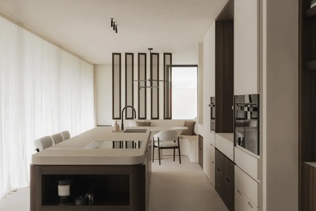 Keuken met afgerond eiland, glazen lamellenscherm en eethoek op de achtergrond, Nieuwbouwwoning in Roeselare, interieur Laura Calleeuw