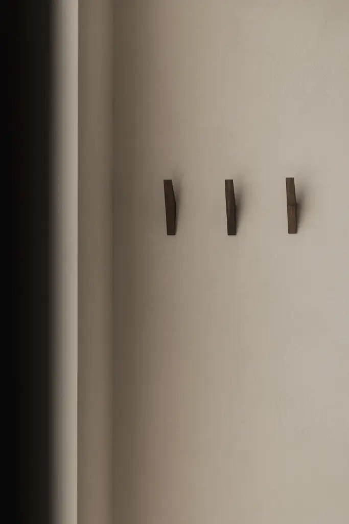 Houten wandhaken tegen een gestucte wand, Nieuwbouwwoning in Roeselare, interieur Laura Calleeuw
