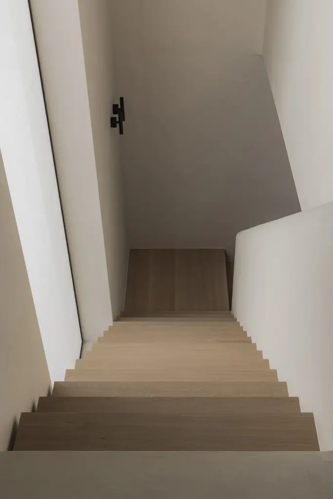 Zwevende eikenhouten trap met travertijn treden en gestucte wand, Nieuwbouwwoning in Roeselare, interieur Laura Calleeuw