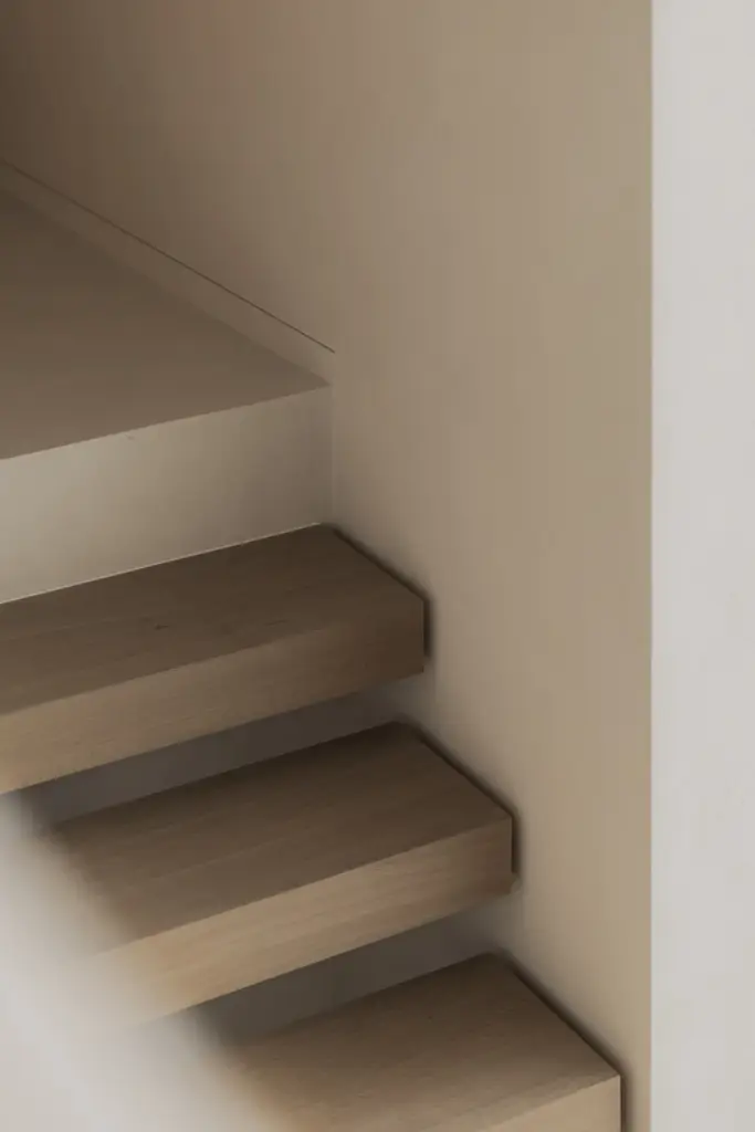 Zwevende eikenhouten trap met travertijn treden en gestucte wand, Nieuwbouwwoning in Roeselare, interieur Laura Calleeuw