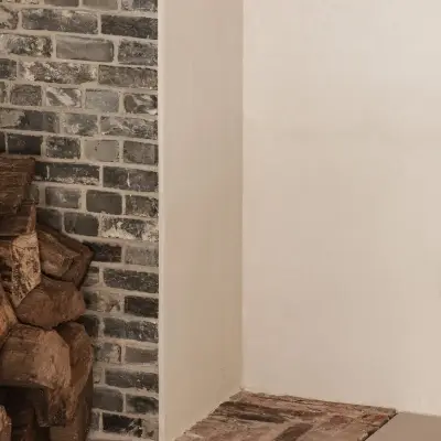 Detail van bakstenen schouw met brandhout en vloer in gebakken tegels, Schuur in Westkapelle, interieur Laura Calleeuw