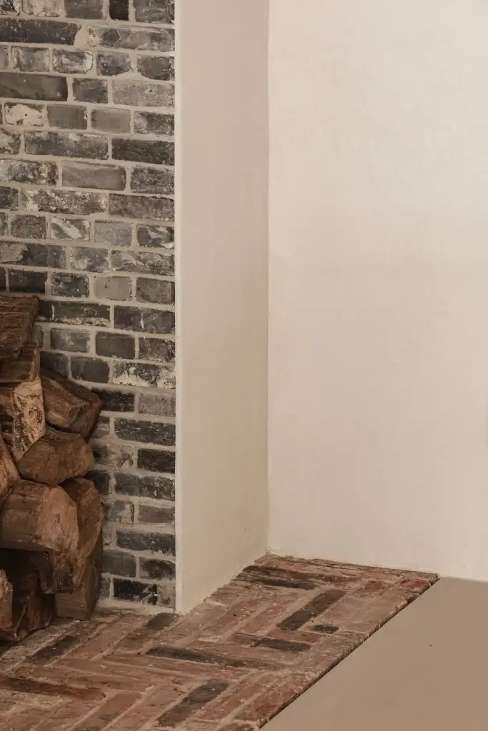 Detail van bakstenen schouw met brandhout en vloer in gebakken tegels, Schuur in Westkapelle, interieur Laura Calleeuw