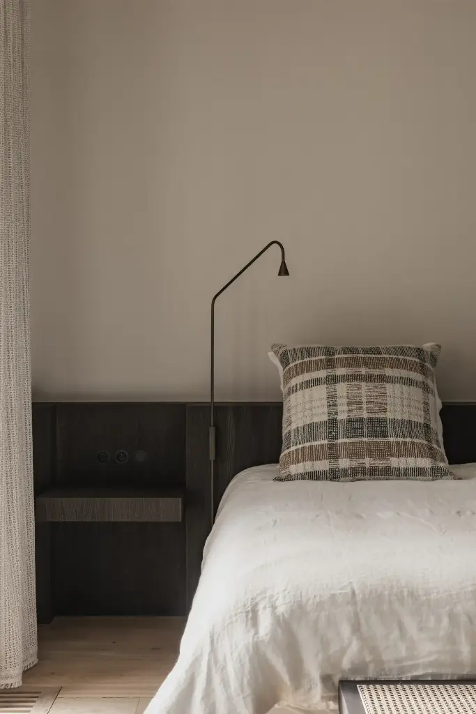 Bed met leeslamp en geruit sierkussen tegen donker eiken hoofdeinde, Schuur in Westkapelle, interieur Laura Calleeuw