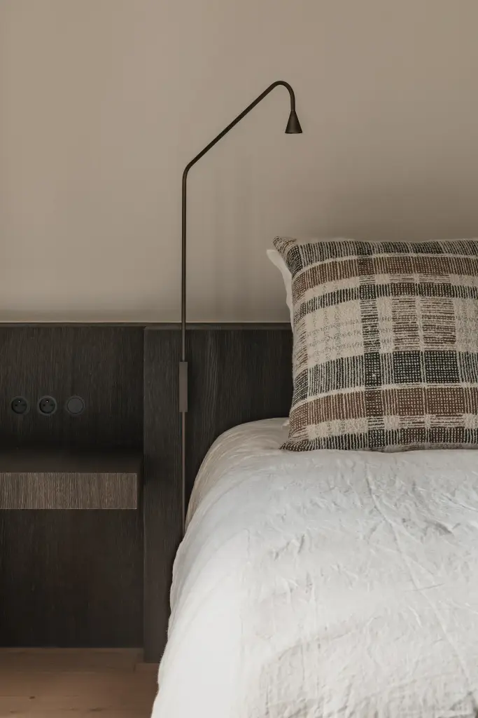 Bed met leeslamp en geruit sierkussen tegen donker eiken hoofdeinde, Schuur in Westkapelle, interieur Laura Calleeuw
