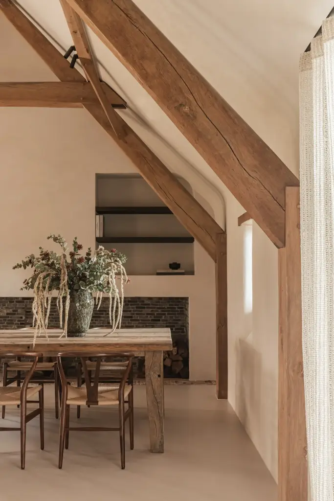 Lange eiktafel onder de eikenhouten spanten met vaas met takken, Schuur in Westkapelle, interieur Laura Calleeuw