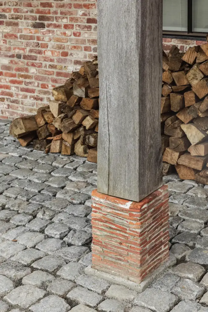 Eikenhouten paal op bakstenen voet met kasseien en gestapeld brandhout, Schuur in Westkapelle, interieur Laura Calleeuw
