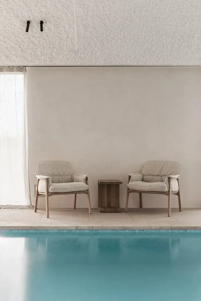 Zithoek met fauteuils en houten bijzettafel naast het zwembad, Schuur in Westkapelle, interieur Laura Calleeuw