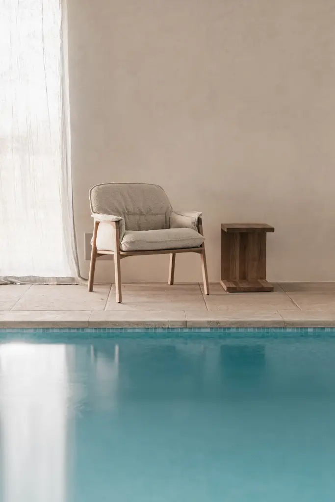 Zithoek met fauteuils en houten bijzettafel naast het zwembad, Schuur in Westkapelle, interieur Laura Calleeuw