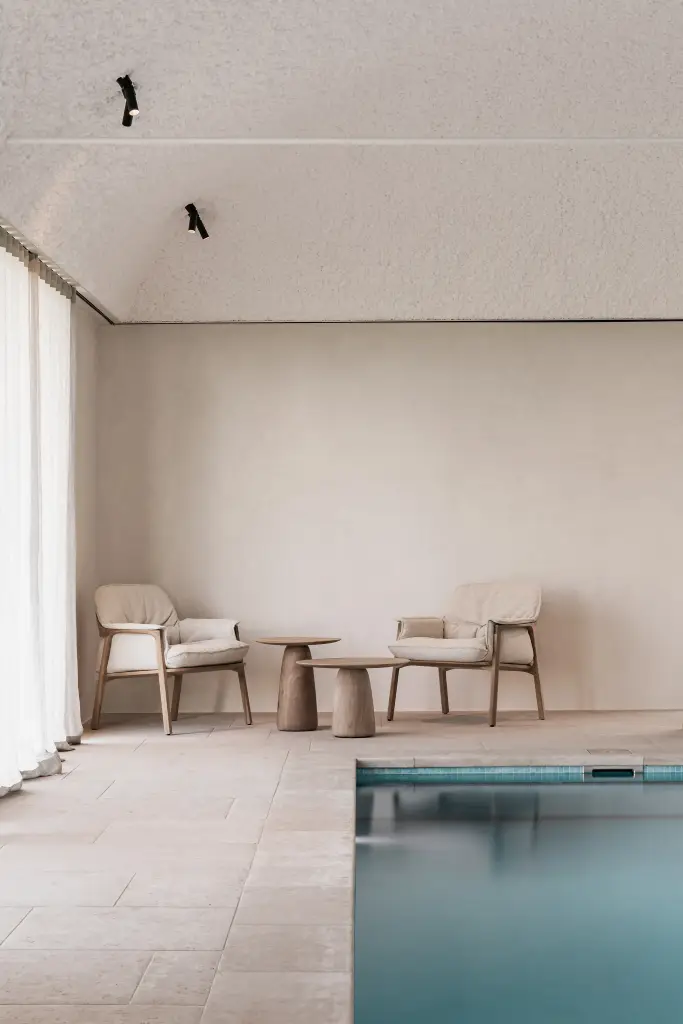 Zithoek met fauteuils en houten bijzettafel naast het zwembad, Schuur in Westkapelle, interieur Laura Calleeuw