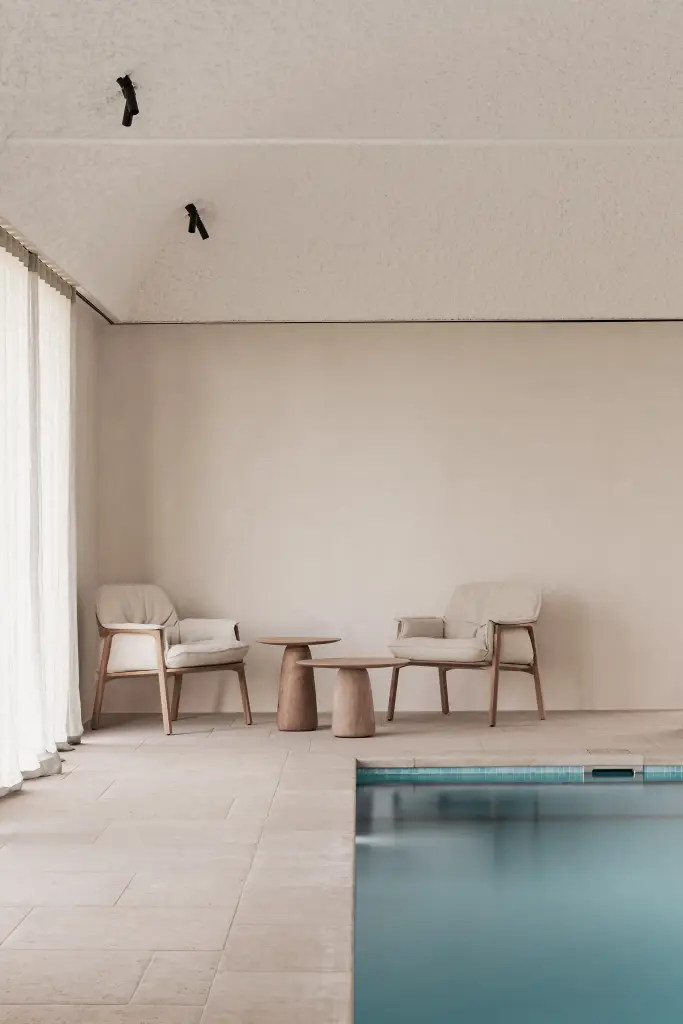 Zithoek met fauteuils en houten bijzettafel naast het zwembad, Schuur in Westkapelle, interieur Laura Calleeuw
