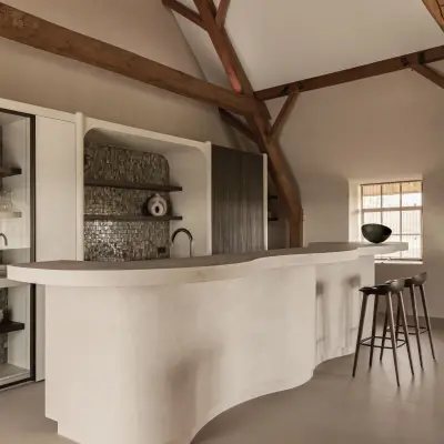 Golvend keukeneiland in microcement met verlichte voet en barkrukken, Schuur in Westkapelle, interieur Laura Calleeuw