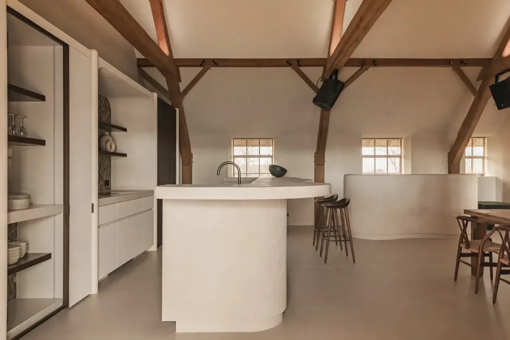 Open keuken in de hoeve met afgerond eiland in microcement onder eikenhouten spanten, Schuur in Westkapelle, interieur Laura Calleeuw