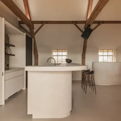 Open keuken in de hoeve met afgerond eiland in microcement onder eikenhouten spanten, Schuur in Westkapelle, interieur Laura Calleeuw