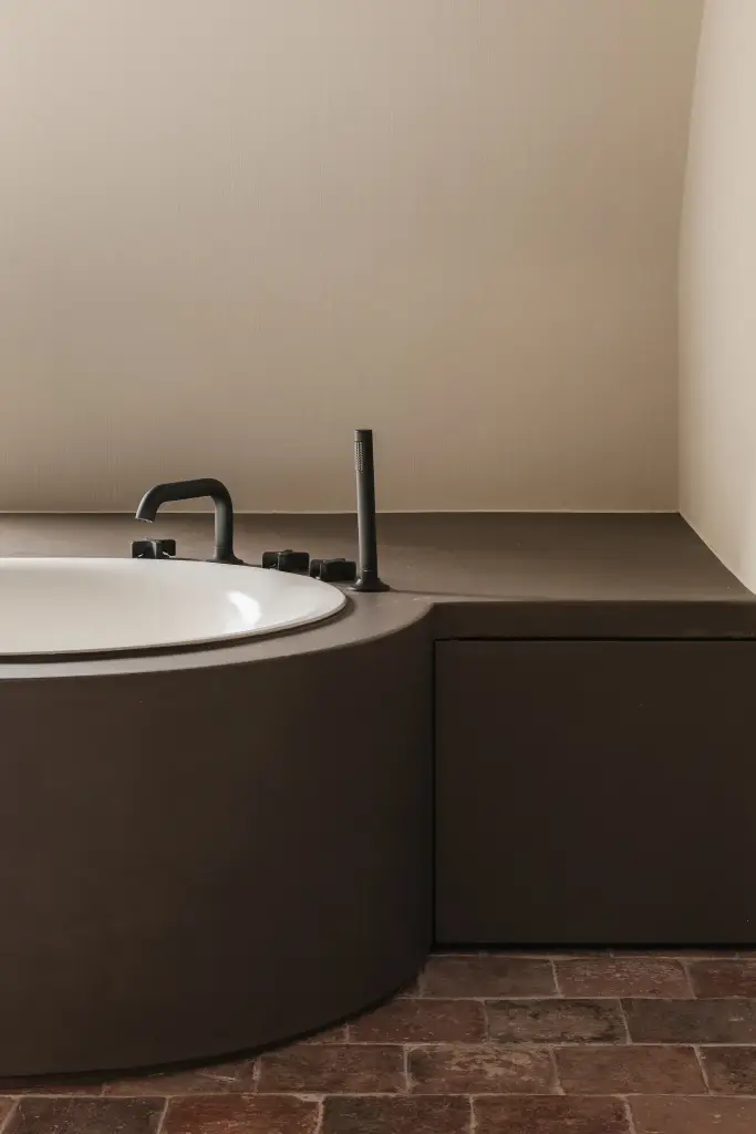 Rond ligbad met donkere omkasting en vloer in gebakken tegels, Schuur in Westkapelle, interieur Laura Calleeuw