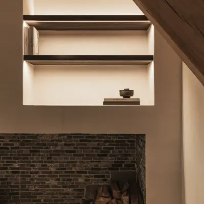 Verlichte nis met donkere planken boven bakstenen haard met brandhout, Schuur in Westkapelle, interieur Laura Calleeuw