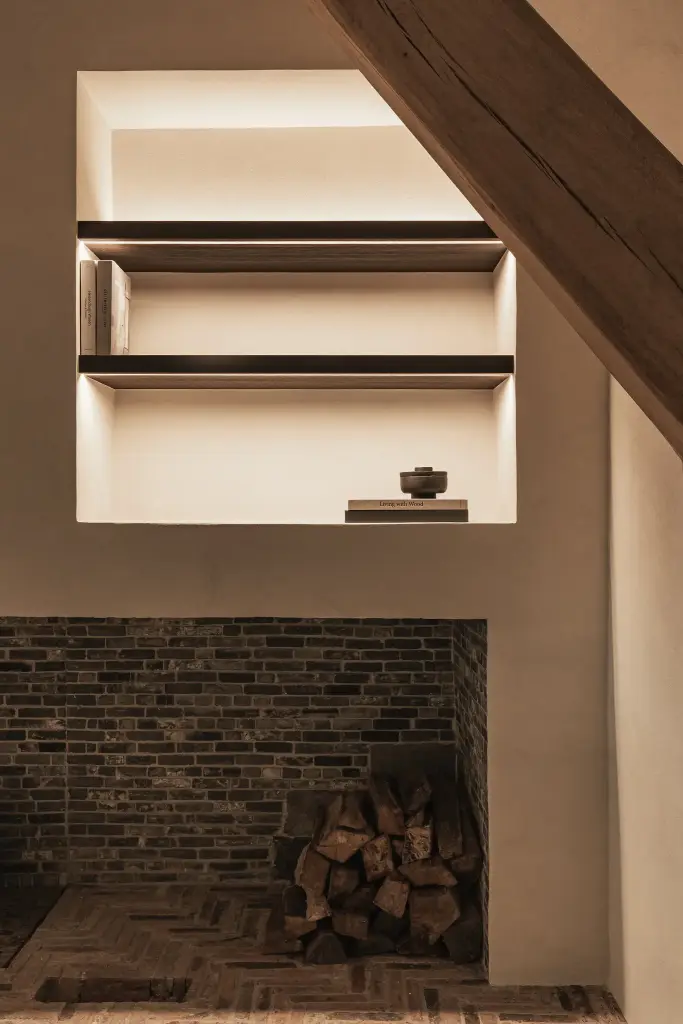 Verlichte nis met donkere planken boven bakstenen haard met brandhout, Schuur in Westkapelle, interieur Laura Calleeuw