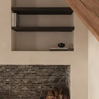 Verlichte nis met donkere planken boven bakstenen haard met brandhout, Schuur in Westkapelle, interieur Laura Calleeuw