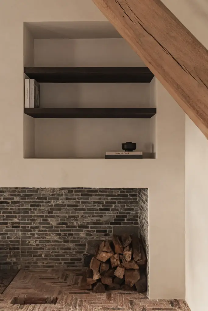 Verlichte nis met donkere planken boven bakstenen haard met brandhout, Schuur in Westkapelle, interieur Laura Calleeuw