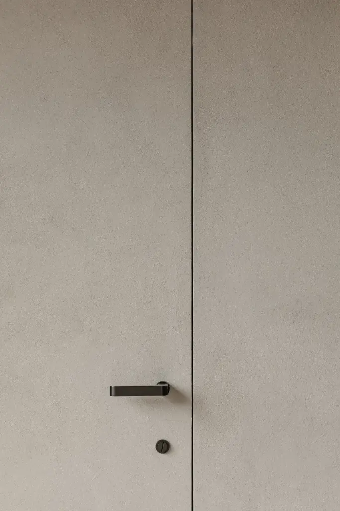 Onzichtbare deur in microcement met zwarte deurklink, Schuur in Westkapelle, interieur Laura Calleeuw
