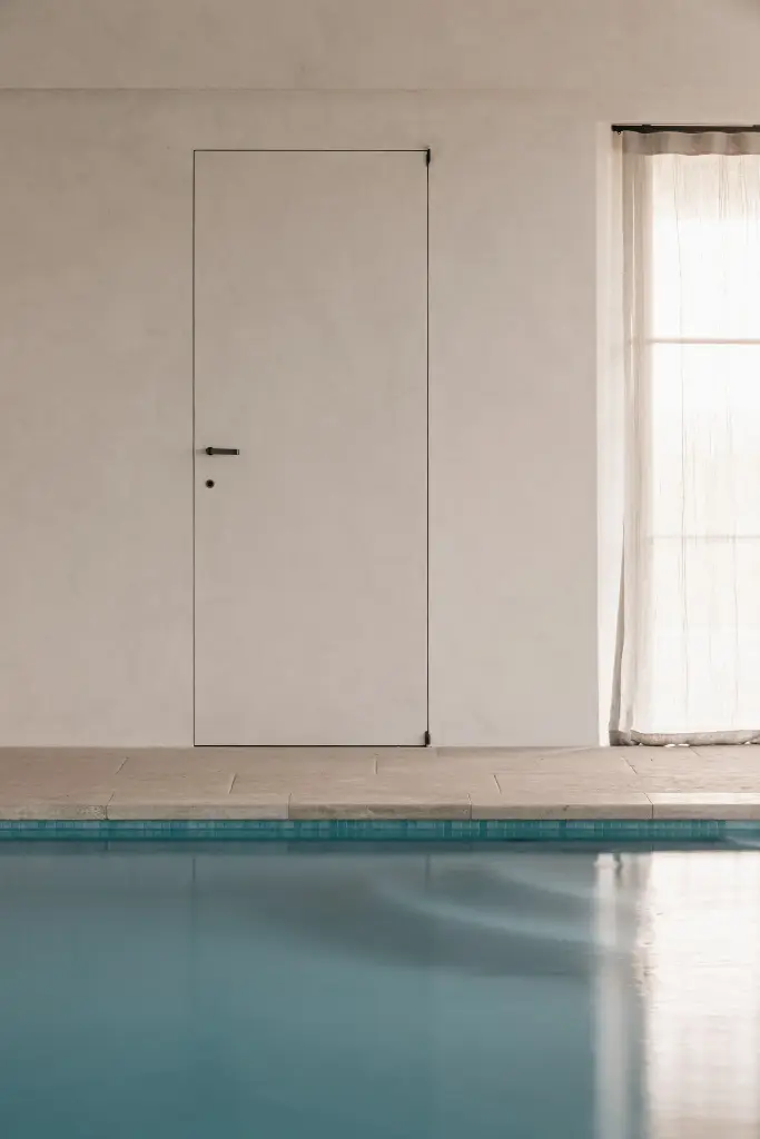 Onzichtbare deur in microcement naast het zwembad, Schuur in Westkapelle, interieur Laura Calleeuw