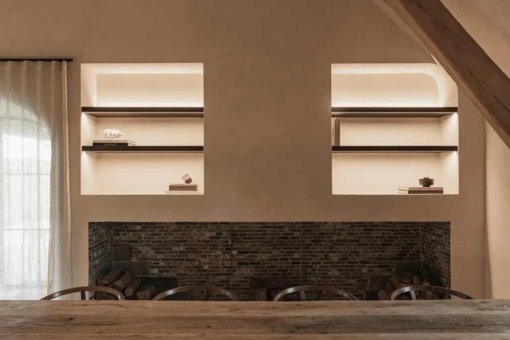 Bakstenen haard met twee nissen met verlichte planken boven een eikenhouten tafel, Schuur in Westkapelle, interieur Laura Calleeuw