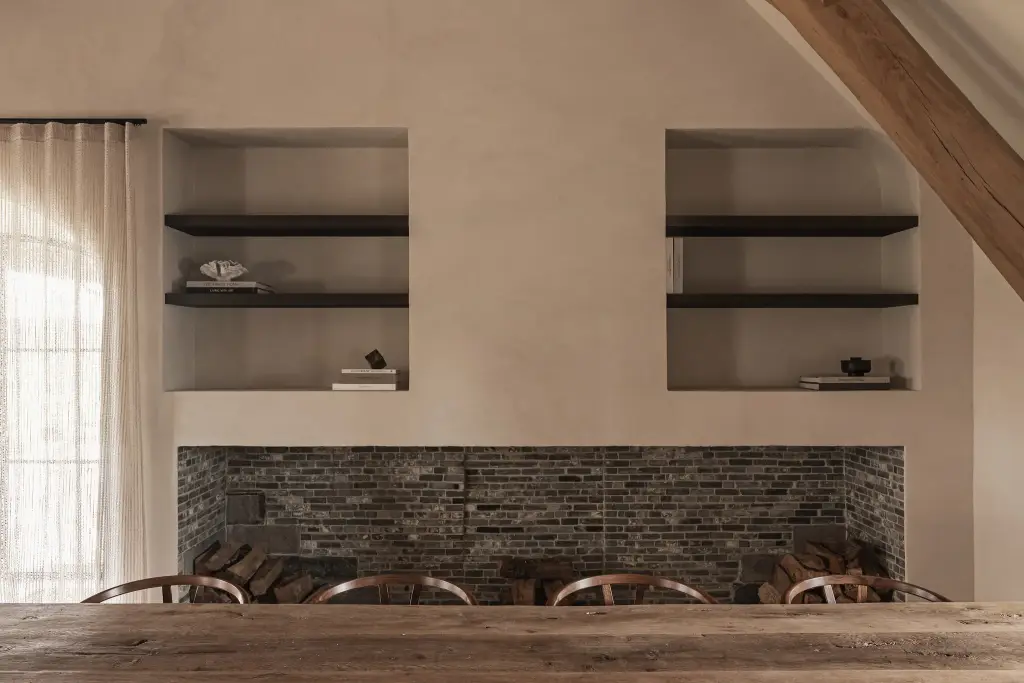 Bakstenen haard met twee nissen met verlichte planken boven een eikenhouten tafel, Schuur in Westkapelle, interieur Laura Calleeuw