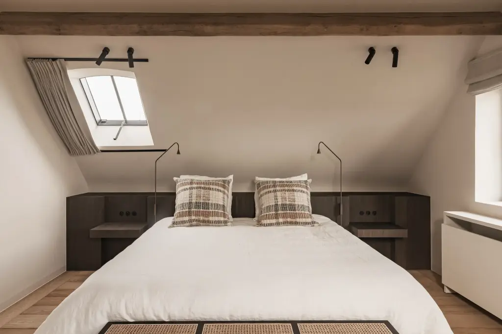 Slaapkamer onder het dak met bed, dakraam en geruite sierkussens, Schuur in Westkapelle, interieur Laura Calleeuw