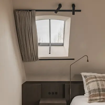 Slaapkamer met leeslamp, donkere nachtkastjes en rolgordijn onder het schuine dak, Schuur in Westkapelle, interieur Laura Calleeuw