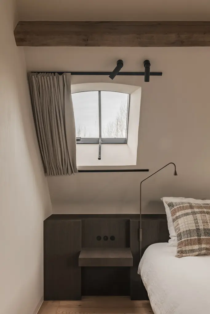 Slaapkamer met leeslamp, donkere nachtkastjes en rolgordijn onder het schuine dak, Schuur in Westkapelle, interieur Laura Calleeuw