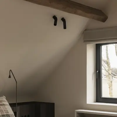Slaapkamer met leeslamp, donkere nachtkastjes en rolgordijn onder het schuine dak, Schuur in Westkapelle, interieur Laura Calleeuw