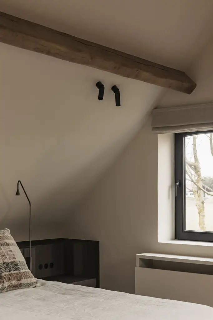 Slaapkamer met leeslamp, donkere nachtkastjes en rolgordijn onder het schuine dak, Schuur in Westkapelle, interieur Laura Calleeuw