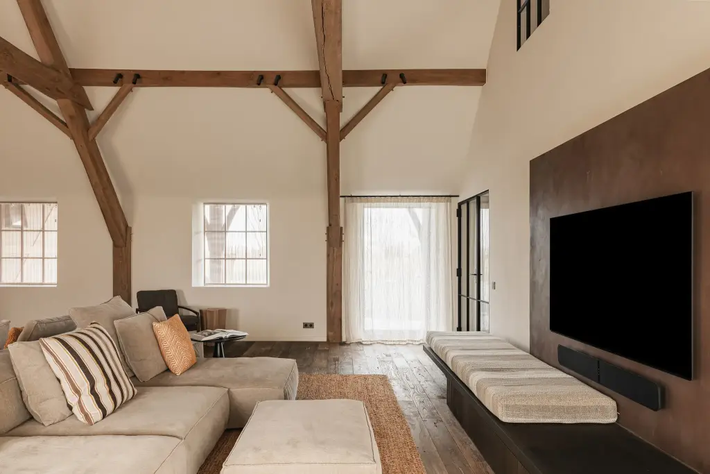 Woonkamer met televisiepaneel in roestkleurig metaal, hoekzetel en eikenhouten spanten, Schuur in Westkapelle, interieur Laura Calleeuw