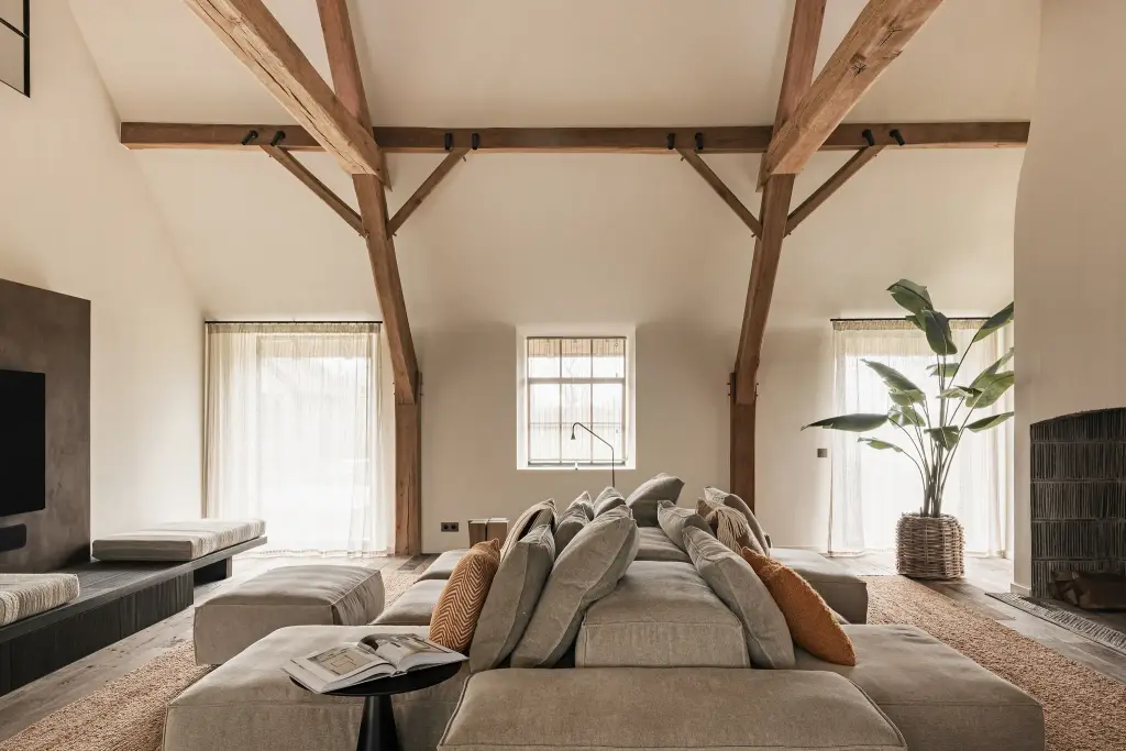 Woonkamer met televisiepaneel in roestkleurig metaal, hoekzetel en eikenhouten spanten, Schuur in Westkapelle, interieur Laura Calleeuw