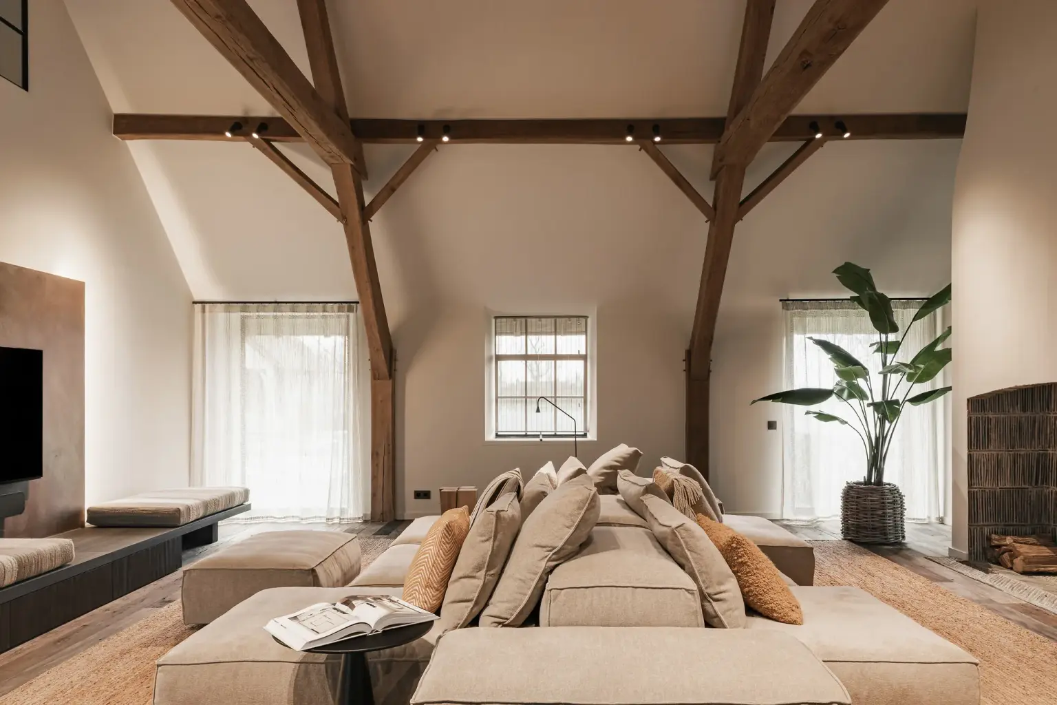 Woonkamer met televisiepaneel in roestkleurig metaal, hoekzetel en eikenhouten spanten, Schuur in Westkapelle, interieur Laura Calleeuw