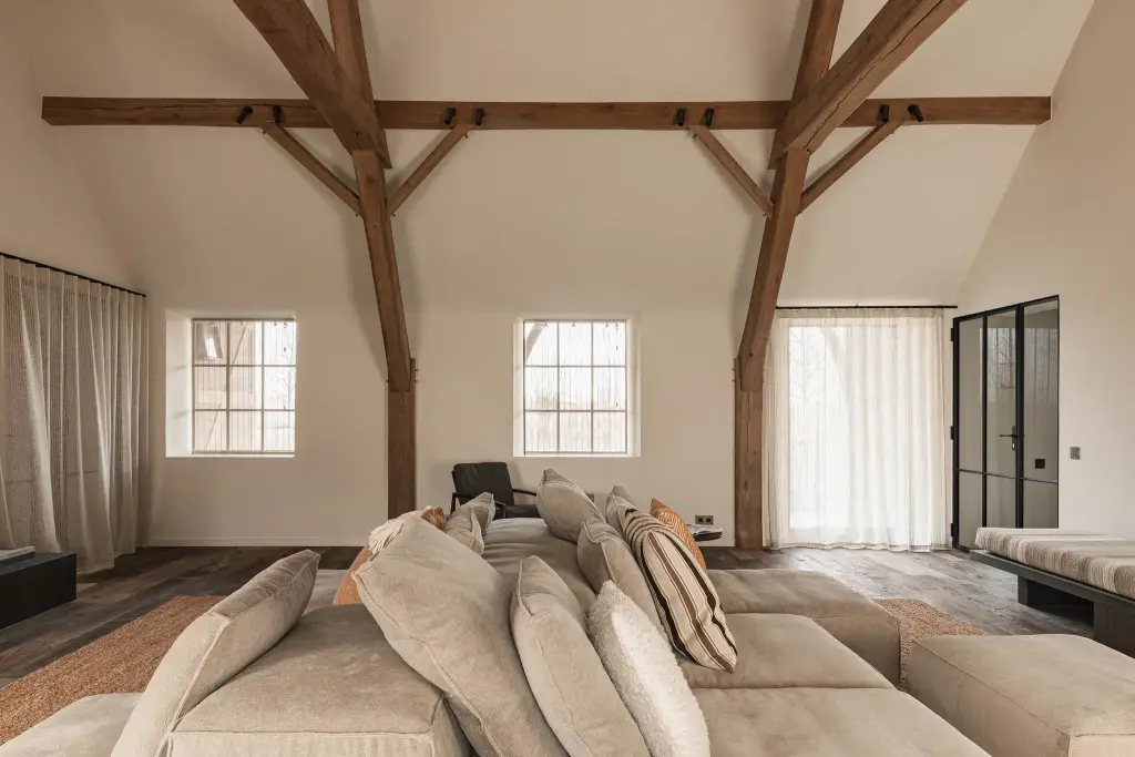 Woonkamer met televisiepaneel in roestkleurig metaal, hoekzetel en eikenhouten spanten, Schuur in Westkapelle, interieur Laura Calleeuw