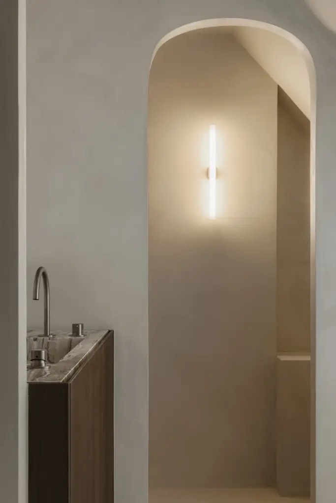 Boogvormige doorgang met wandlamp naast een wastafel op een houten onderkast, Het Zoute Schorre, interieur Laura Calleeuw