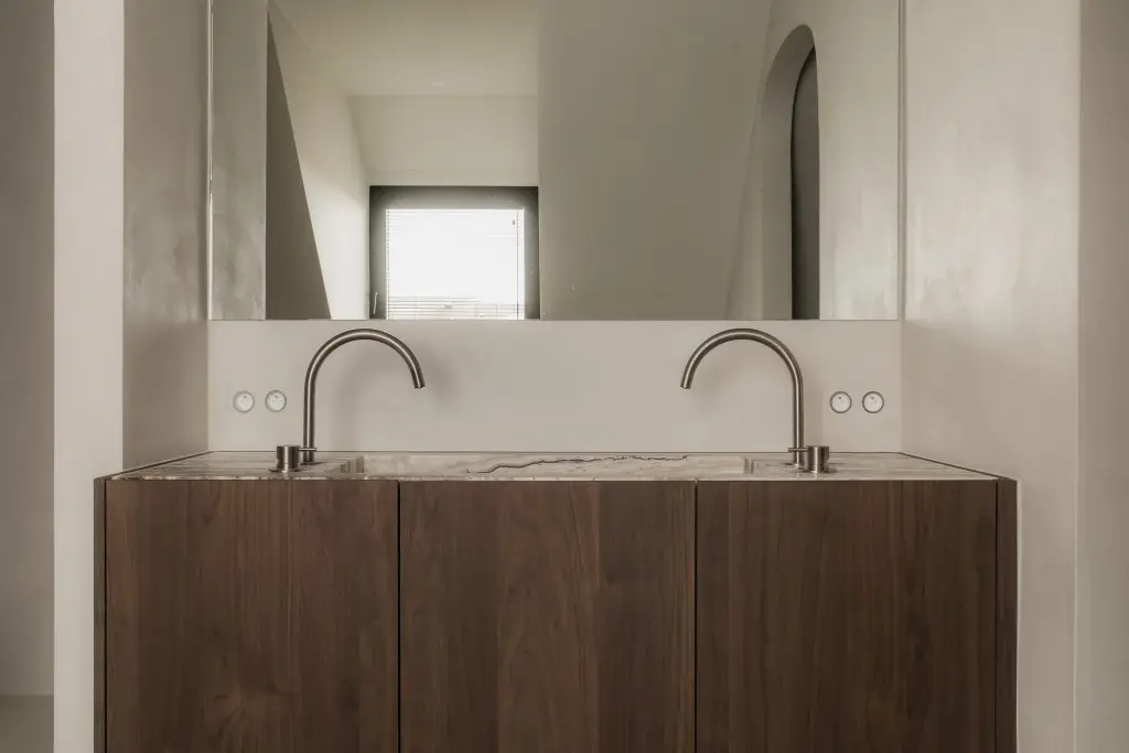Dubbele wastafel met twee kranen onder een brede spiegel, op een houten onderkast, Het Zoute Schorre, interieur Laura Calleeuw