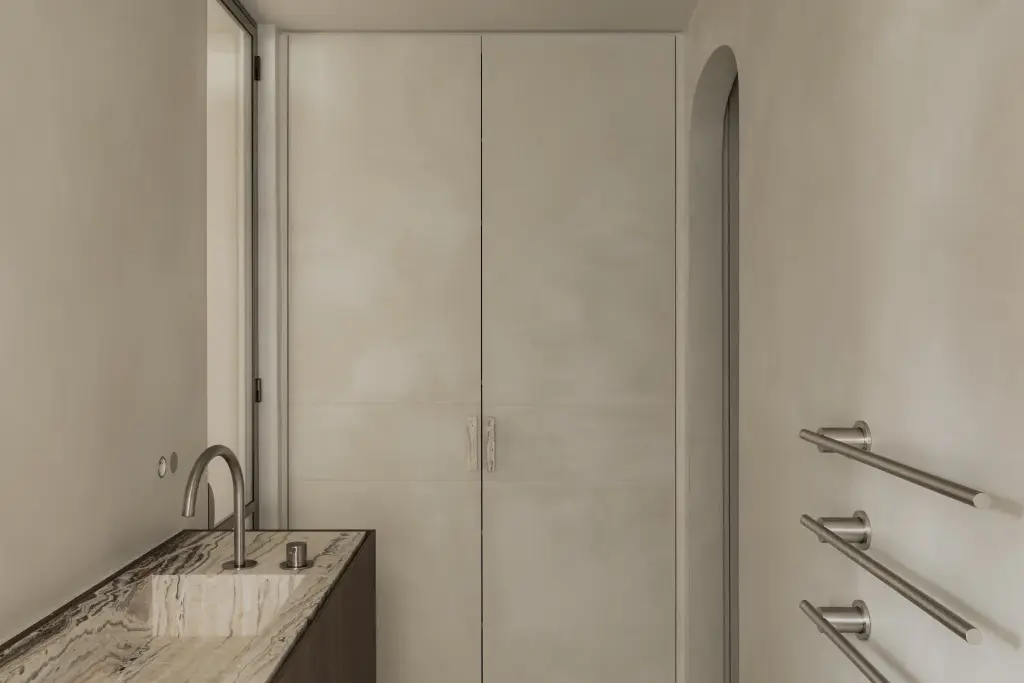 Wastafel met kraan naast kastdeuren, een handdoekradiator en een boogvormige nis, Het Zoute Schorre, interieur Laura Calleeuw