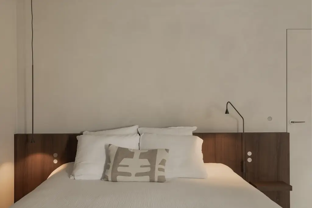 Bed met houten hoofdbord, kussens met grafisch patroon en een wandlamp, Het Zoute Schorre, interieur Laura Calleeuw