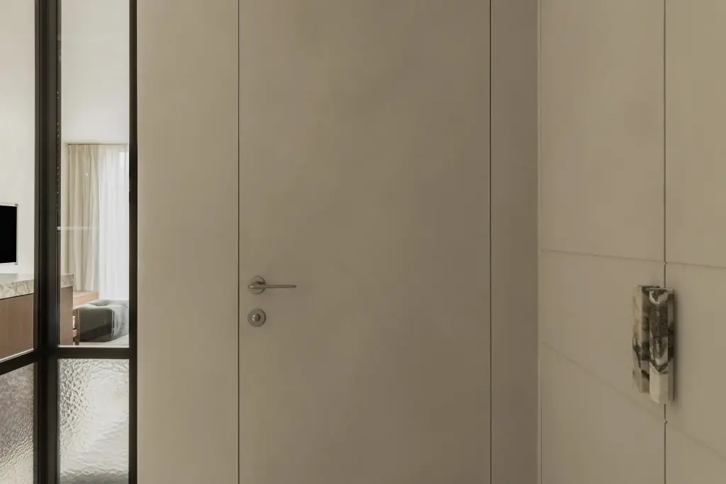 Inkom met vlakke deur in een gladde pleisterwand en een kastdeur met natuurstenen handgreep naast een stalen glaswand, Het Zoute Schorre, interieur Laura Calleeuw